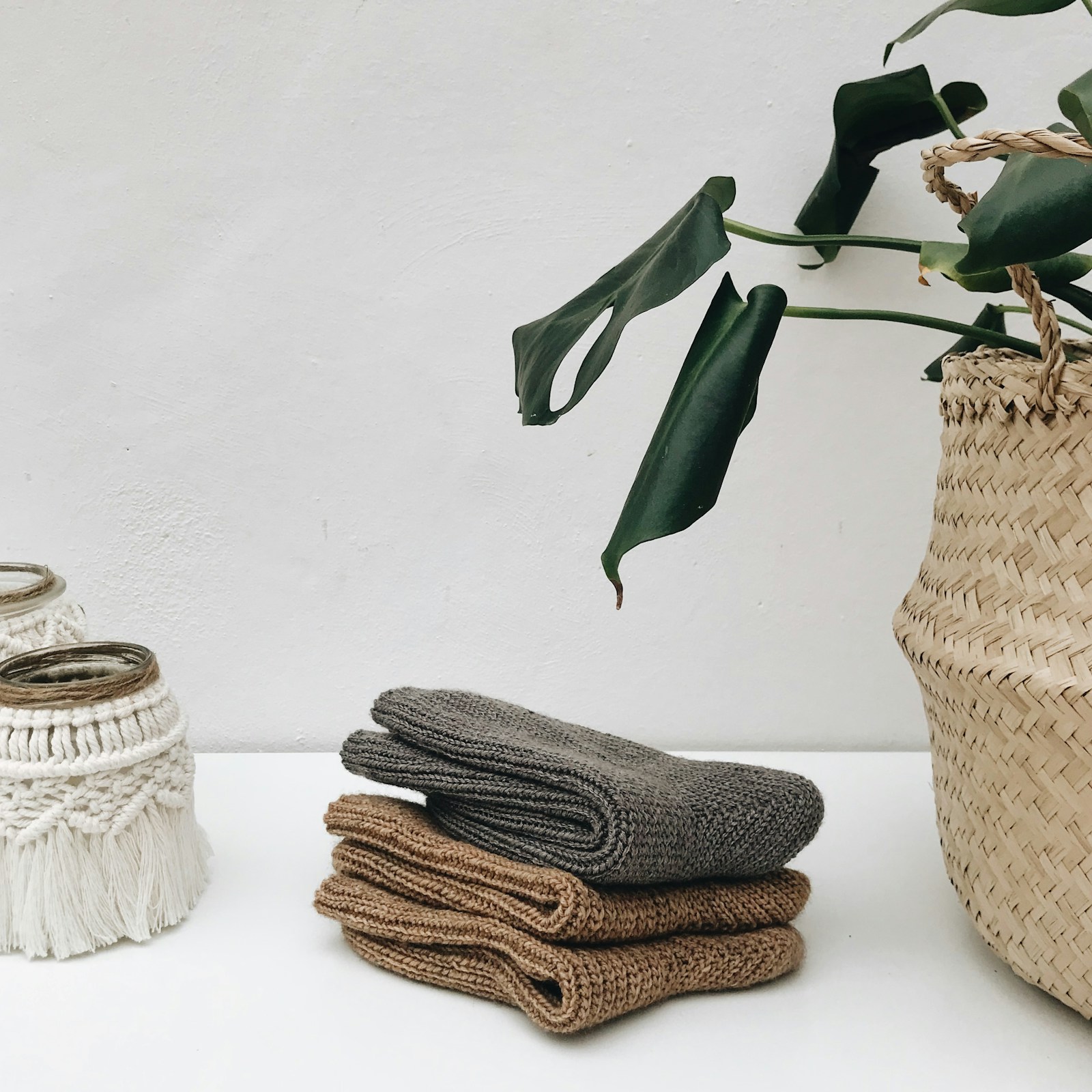 Folded knitted blankets stacked beside a woven basket in a bright room